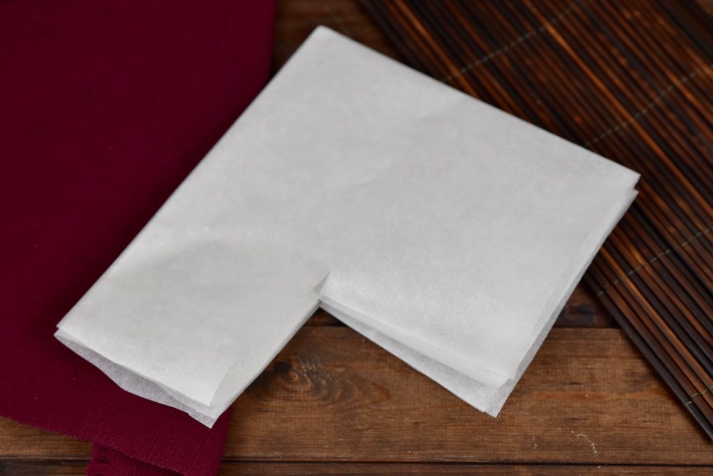 Ein Blatt weißes Backpapier 2 mal gefaltet. An einer Ecke ist ein Stück rausgeschnitten. Hintergrund dunkel.