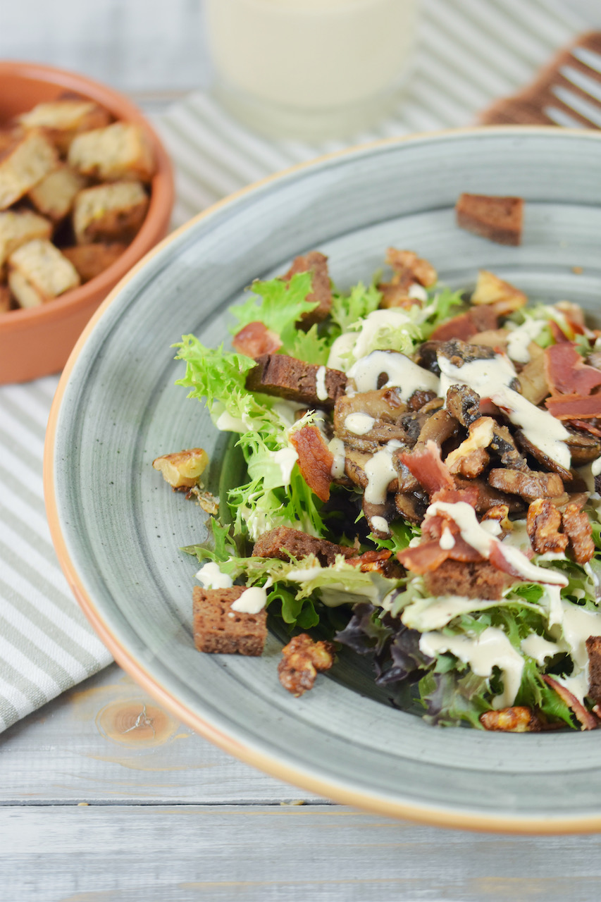 Veganer Caesar Salad mit Pilzen und Walnüssen auf grauem Teller. Hintergrund hell.