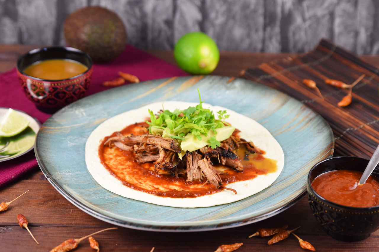 Mexikanische Carnitas mit Salsa de Chipotle, Avocado und Koriander auf Tortilla. Hintergrund dunkel.