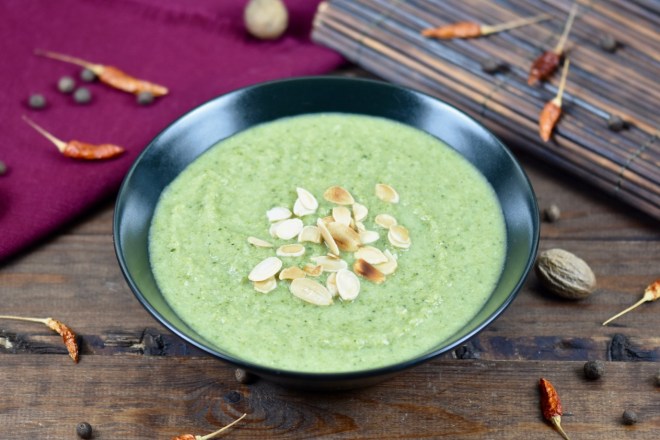 cremige Brokkolisuppe in schwarzer Schale, dekoriert mit Mandelplättchen. Hintergrund dunkel