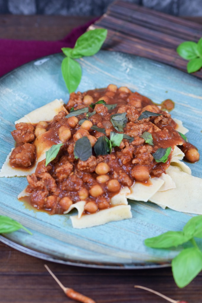 Pasta mit Salsiccia und Kichererbsen auf blauem Teller. Hintergrund dunkel.