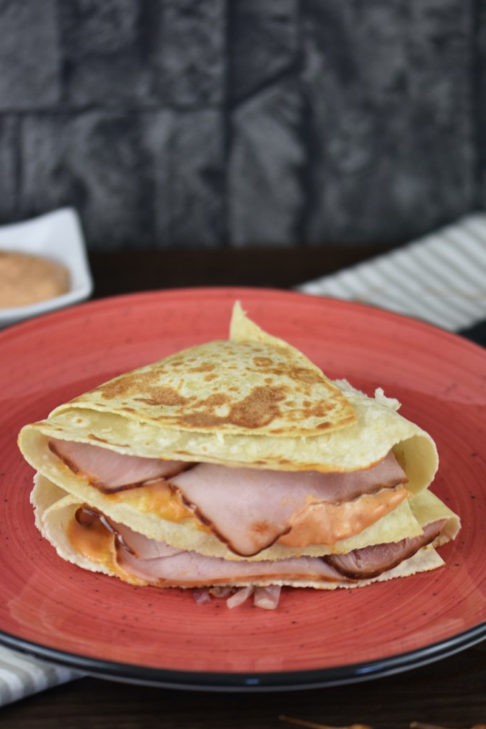 Reuben Sandwich-Tortilla Wrap auf rotem Teller. Hintergrund dunkel.