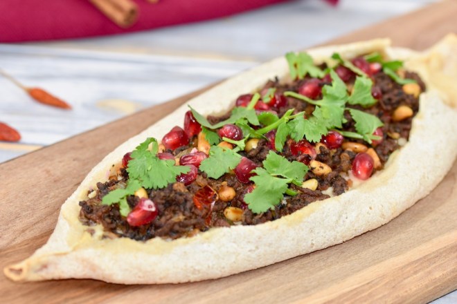 Pide mit Zimt-Hackfleisch, garniert mit Koriandergrün, auf einem Holzbrett.