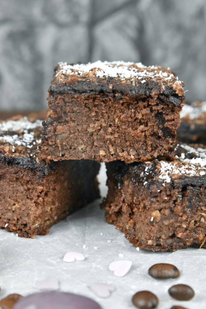 Vegane Brownies übereinander gestapelt auf Backpapier. Hintergrund dunkel.