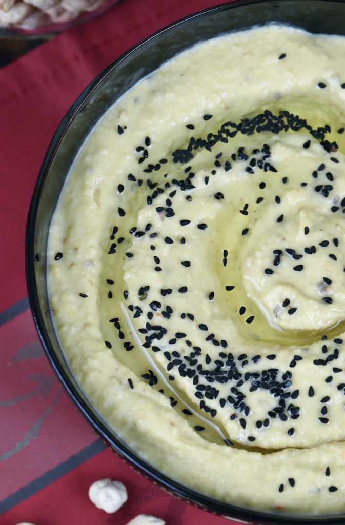 Klassisches Hummus aus Israel mit Schwarzkümmelsamen garniert. Es ist in einer schwarzen Schale und der Hintergrund ist dunkel.