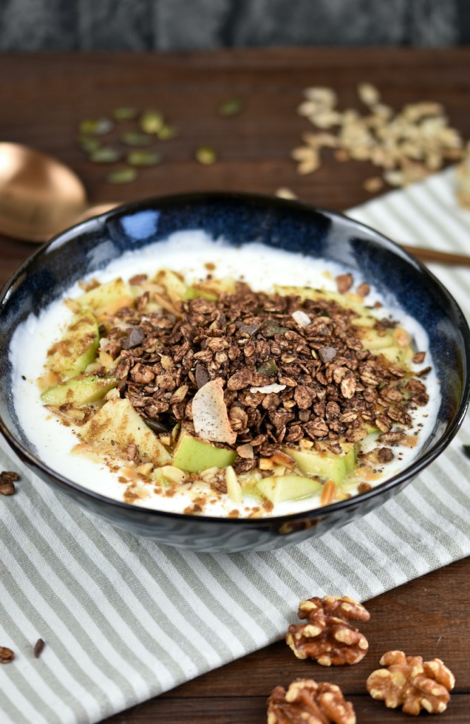Schokoladen Granola in einer Schüssel mit Joghurt und Äpfeln.
