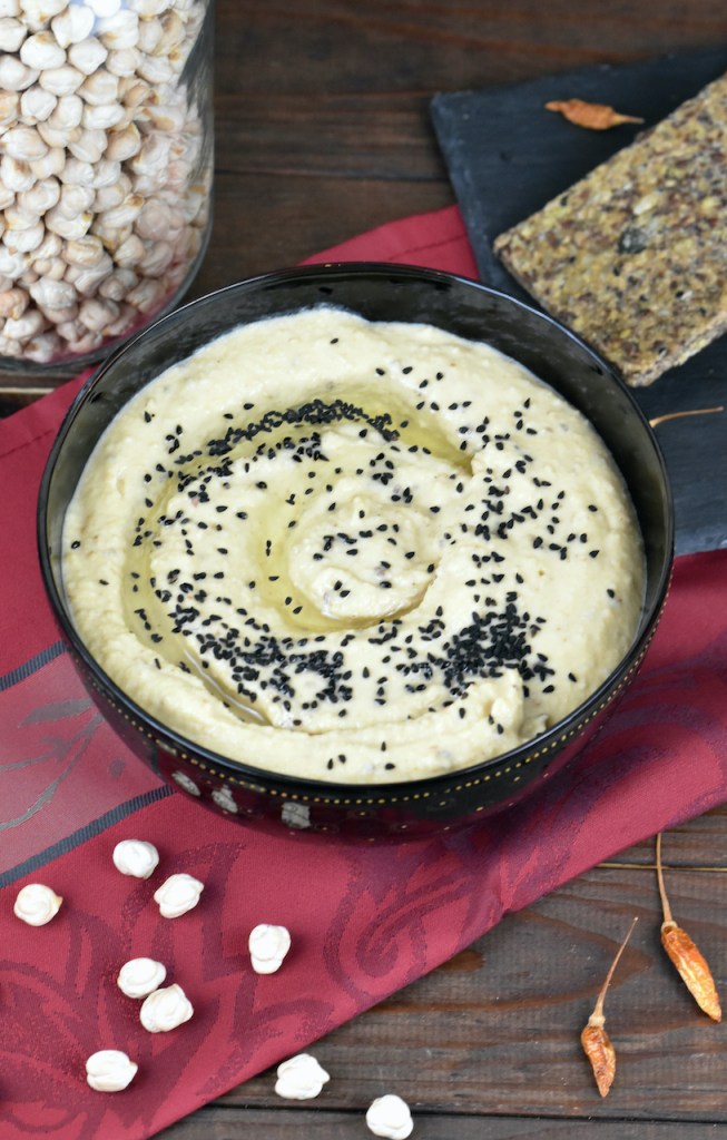 Klassisches Hummus aus Israel mit Schwarzkümmelsamen garniert. Es ist in einer schwarzen Schale und der Hintergrund ist dunkel.