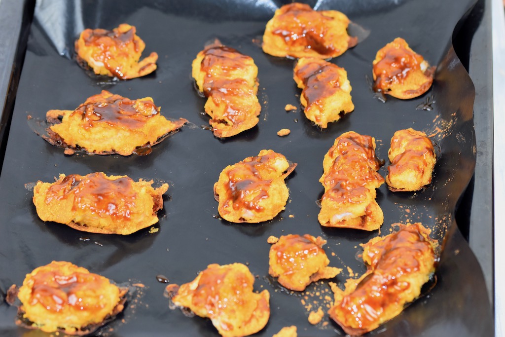 Hähnchennuggets im Teigmantel bestrichen mit Hoisin-Sauce auf einem Backblech.