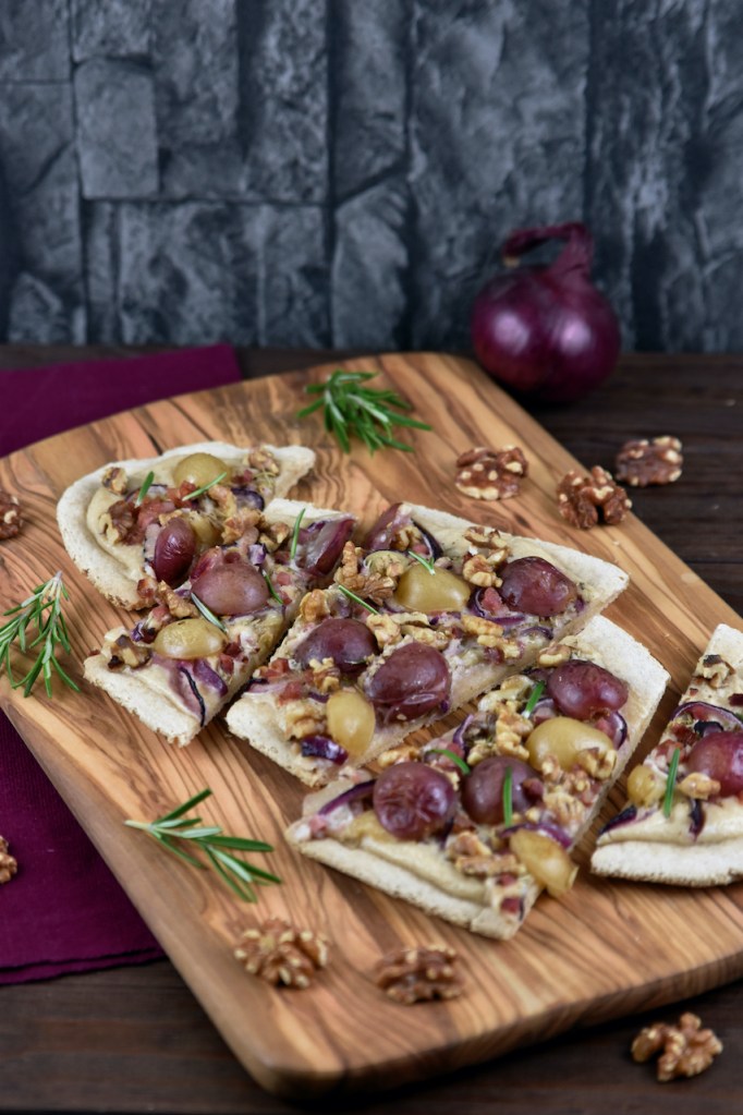 Flammkuchen mit Weintrauben und Walnüssen in Stücke geschnitten auf einem Holzbrett.