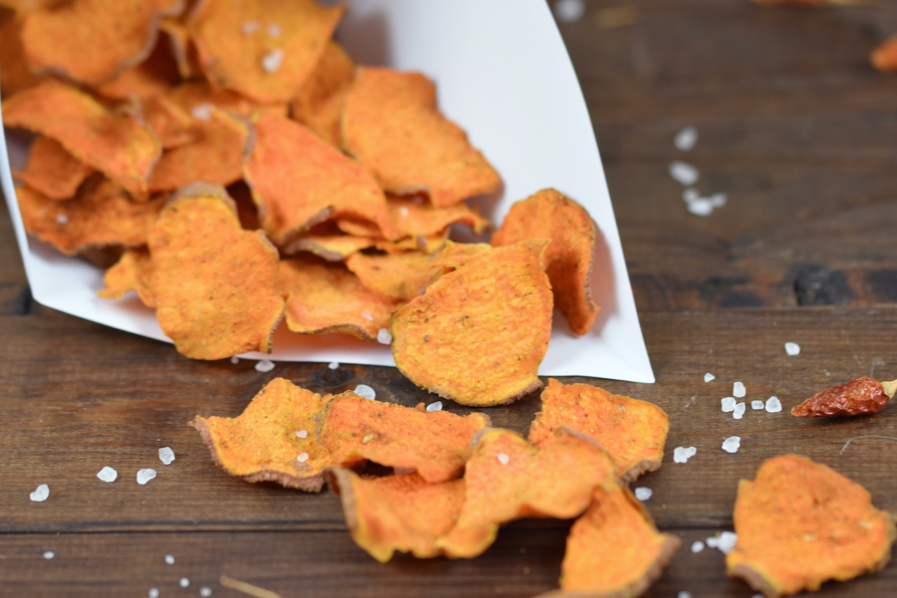 Knusprige Süßkartoffelchips mit BBQ-Aroma in einer Papiertüte. Hintergrund dunkel.