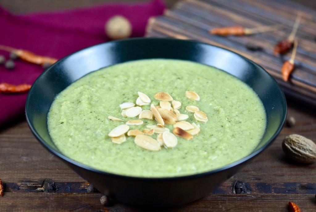 cremige Brokkolisuppe in schwarzer Schale, dekoriert mit Mandelplättchen. Hintergrund dunkel
