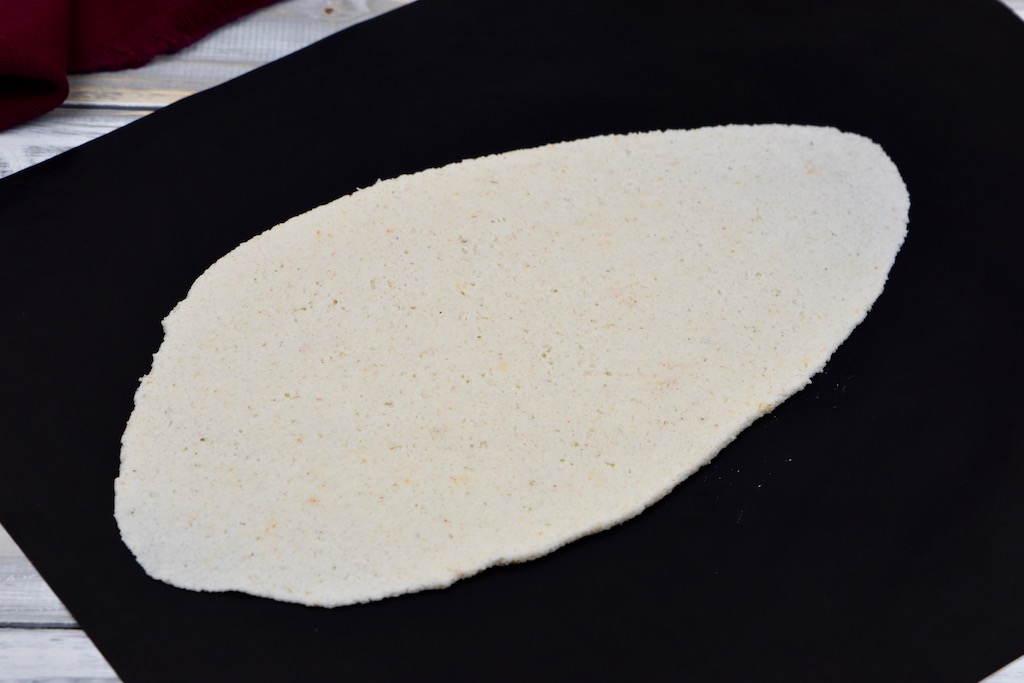 Zu einem länglichen Fladen ausgerollter Pizzateig. Hintergrund schwarz.