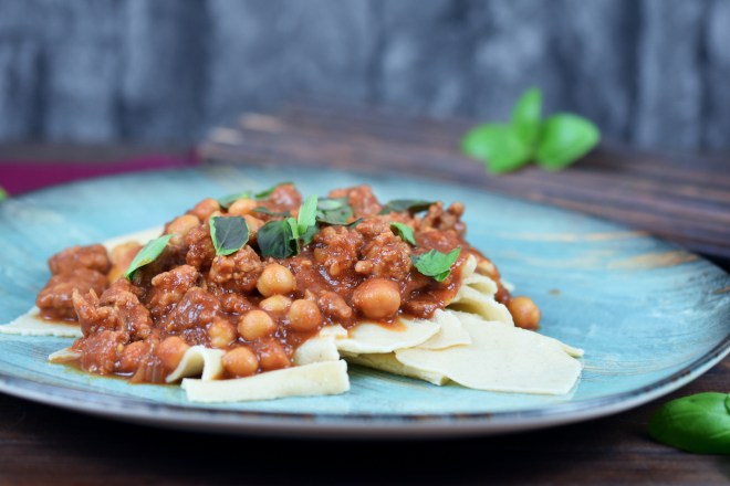 Pasta mit Salsiccia und Kichererbsen auf blauem Teller. Hintergrund dunkel.