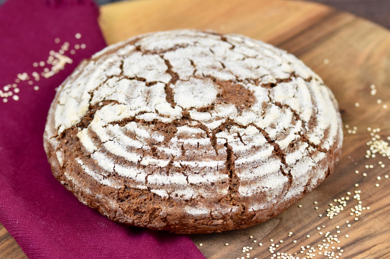 glutenfreies Krustenbrot in rund auf Holzbrett. Dekoriert ist es mit einer weinroten Stoffserviette und groben Salzkörnern.