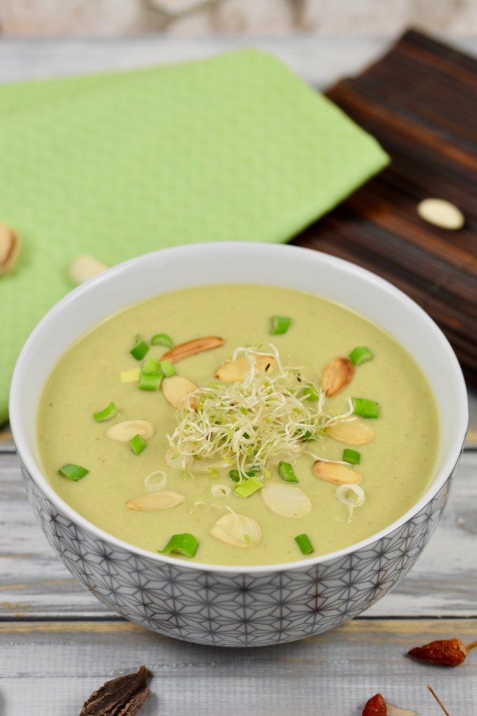 Schnelle Erbsensuppe in Porzellanschale, garniert mit Mandelplättchen, Frühlingszwiebeln und Sprossen. Hintergrund hell.