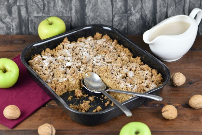 Apple Crumble mit Walnüssen und Haferflocken in einer Auflaufform. Hintergrund dunkel.