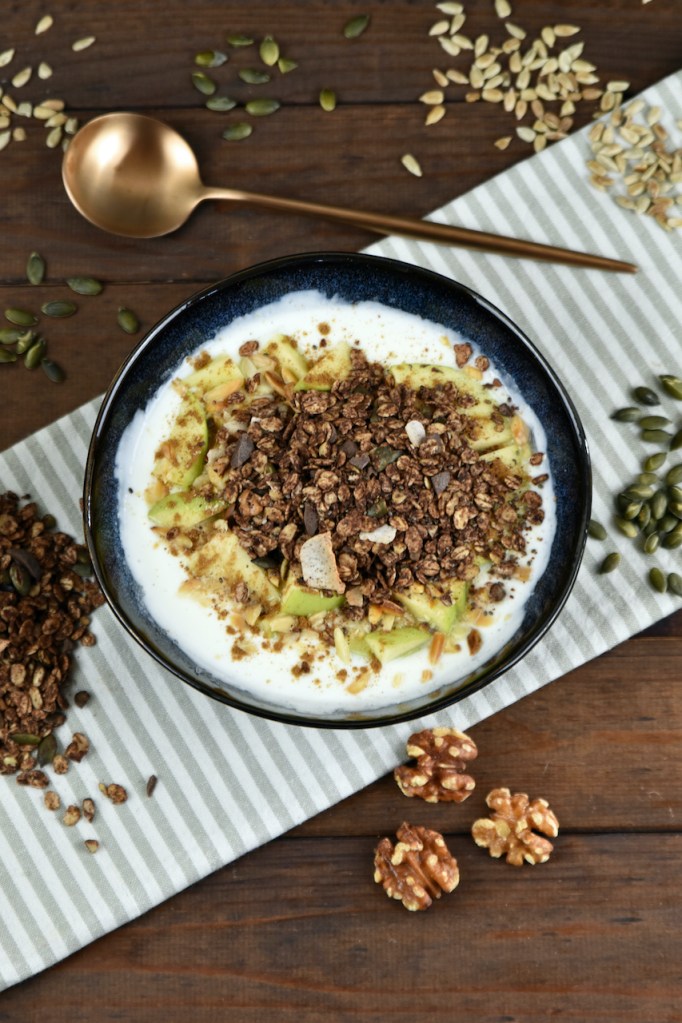 Schokoladen Granola in einer Schüssel mit Joghurt und Äpfeln.