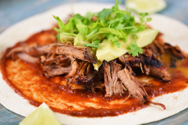 Mexikanische Carnitas mit Salsa de Chipotle, Avocado und Koriander auf Tortilla. Hintergrund blau.