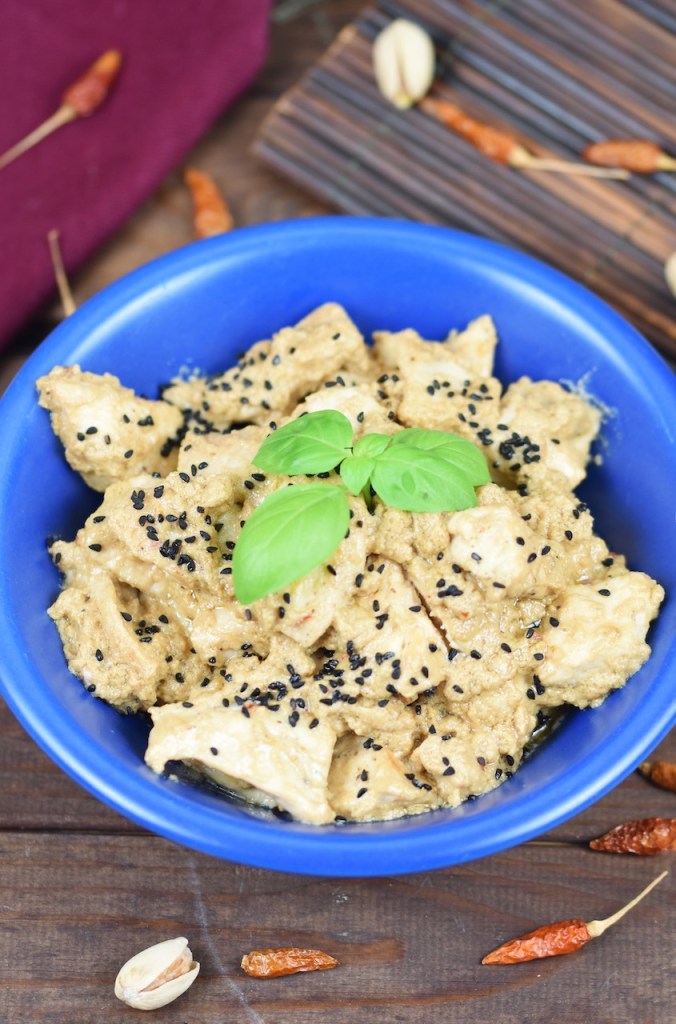 Hähnchen-Mezze in Tahini-Kokossauce in einer blauen Schale garniert mit Basilikum. Hintergrund dunkel.