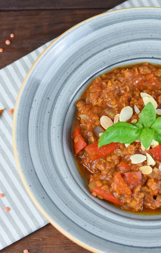 Italienischer Eintopf mit Tomaten, Paprika und Linsen in grauem Teller. Hintergrund dunkel.