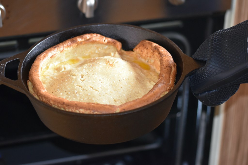 Glutenfreier Dutch Baby im schwarzen Gusseisentopf wird gerade aus dem Ofen geholt.