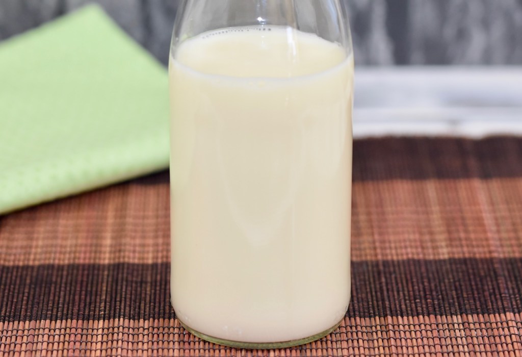 Milch in Glasflasche, Hintergrund braun und hellgrün