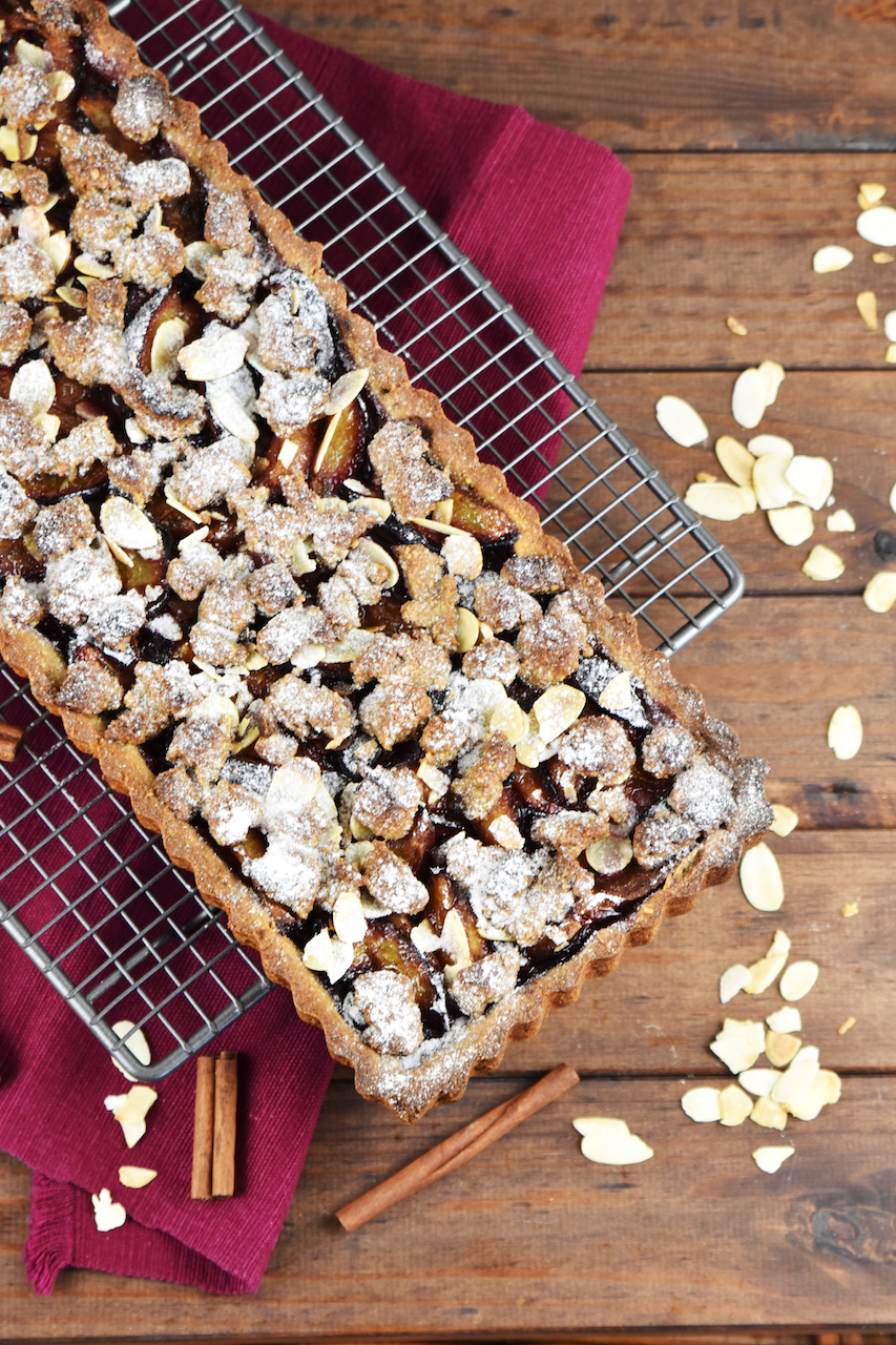 Glutenfreie Pflaumen-Tarte mit Zimtstreuseln. Hintergrund dunkel.