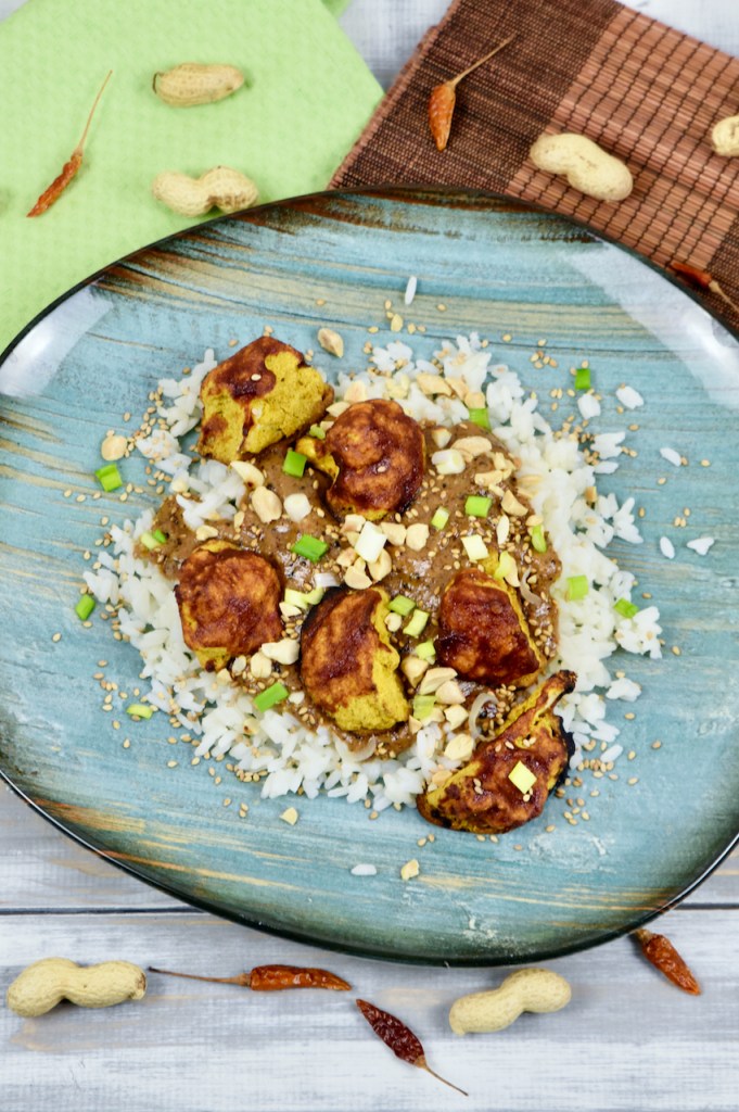 Knusprige Blumenkohlröschen mit Erdnusssauce und Reis, garniert mit Erdnüssen und Frühlingszwiebeln.