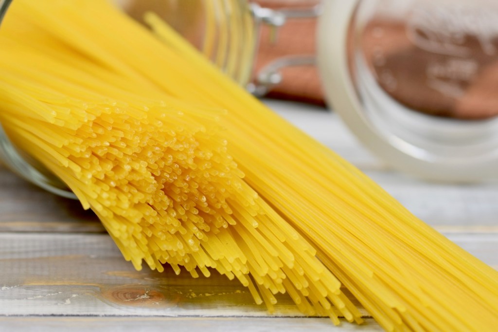 Spaghetti in einem Glas liegend. Die Spaghetti sind leicht aus dem Glas rausgerutscht. Hintergrund hell.