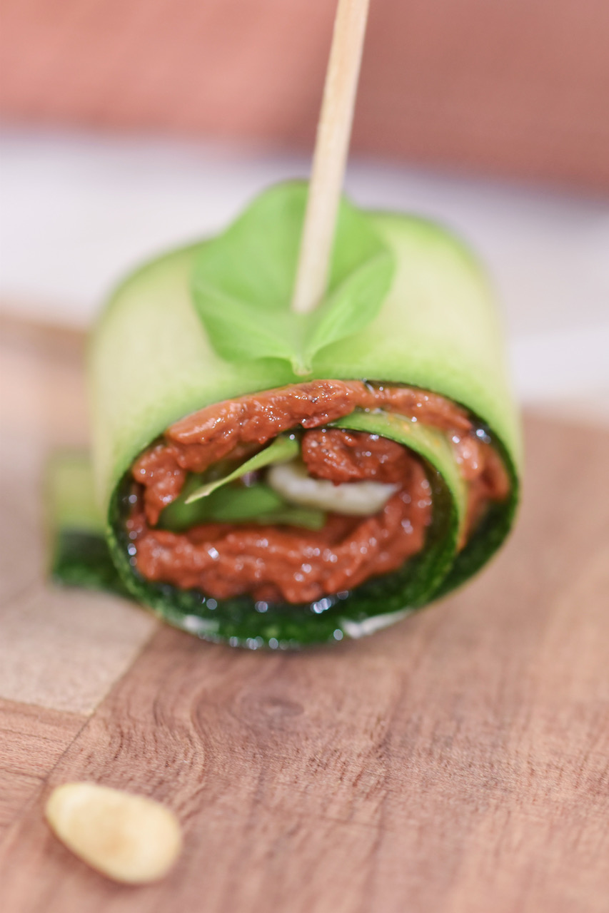 Zucchini-Röllchen mit Paprikacreme und Pinienkernen gefüllt auf Holzbrett.