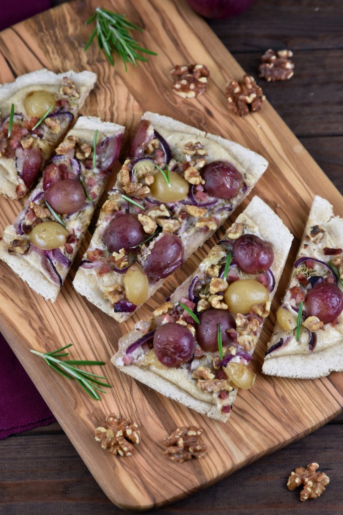 Flammkuchen mit Weintrauben und Walnüssen in Stücke geschnitten auf einem Holzbrett.