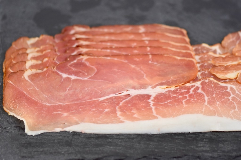 In Scheiben geschnittener Schinken auf Schieferplatte.