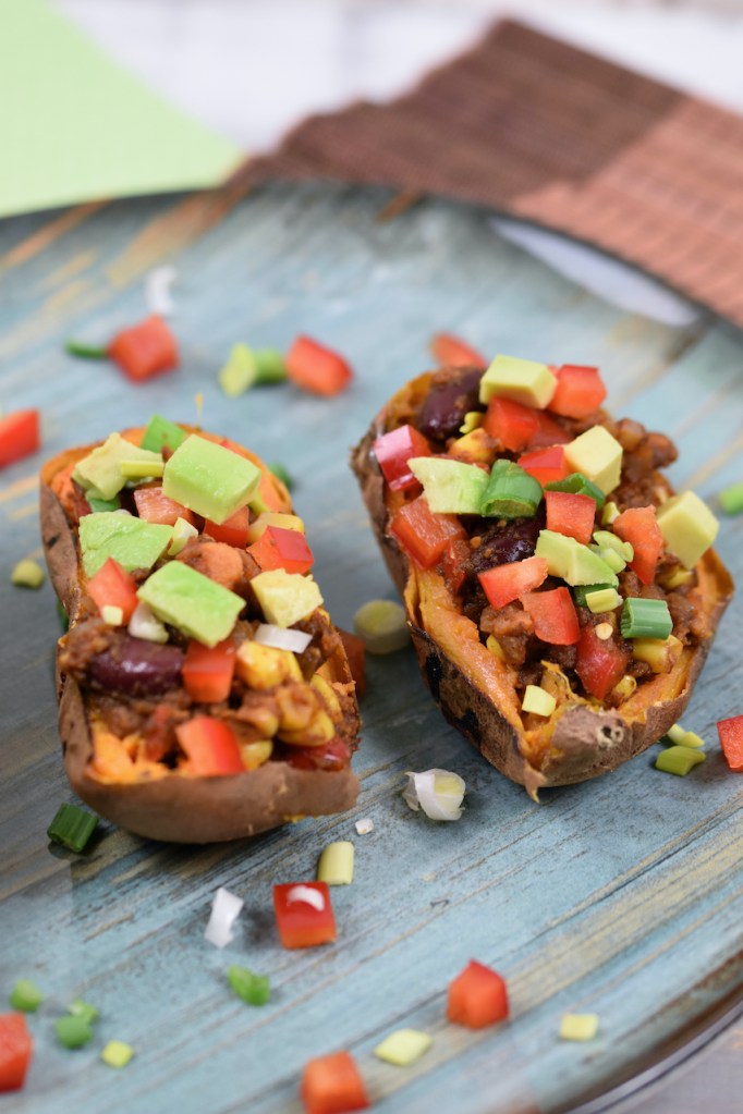 Gefüllte Süßkartoffel auf mexikanische Art dekoriert mit Paprika, Avocado und Frühlingszwiebeln.