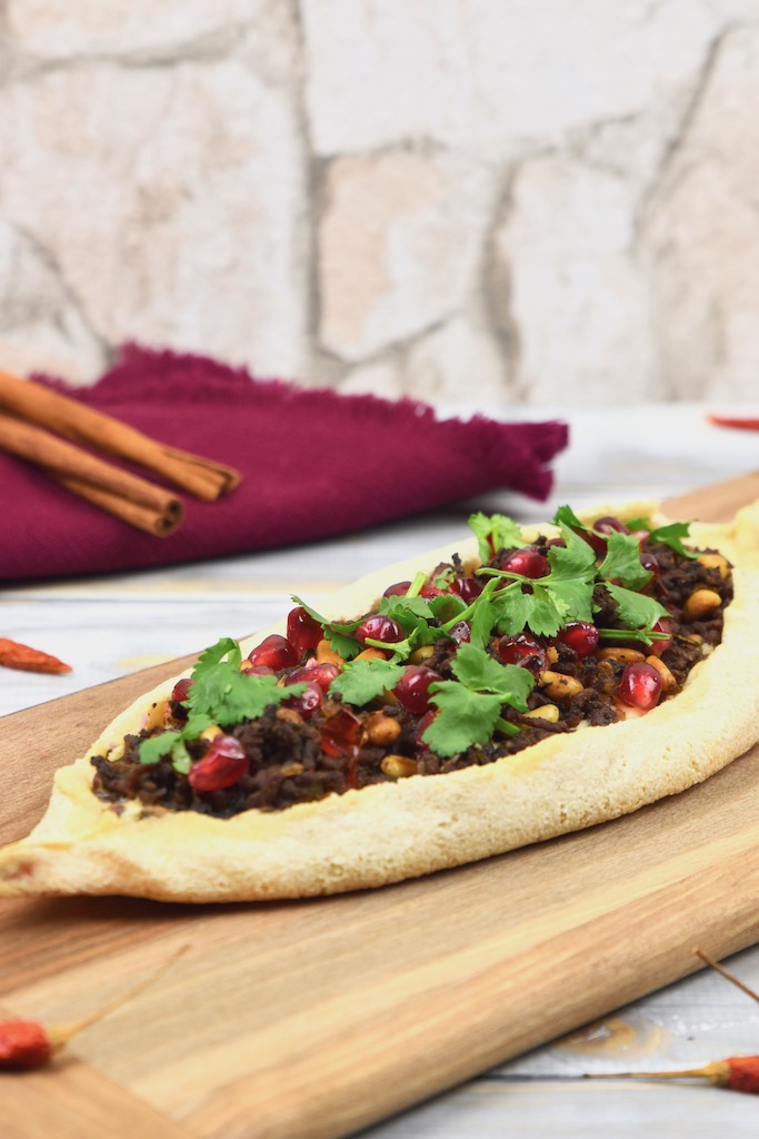 Pide mit Zimt-Hackfleisch, garniert mit Koriandergrün, auf einem Holzbrett.