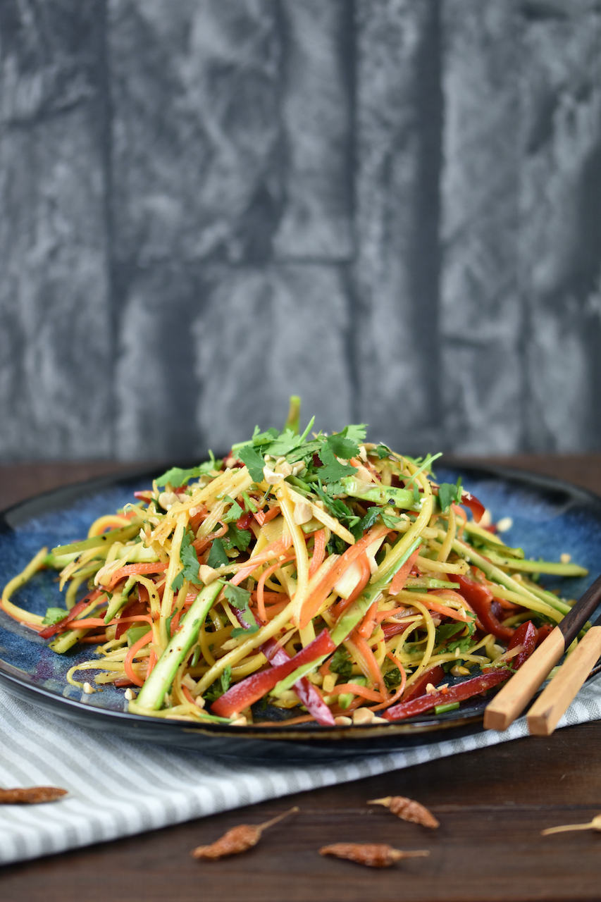 Thai Salat mit Mango und gerösteten Erdnüssen auf einem blauen Teller.