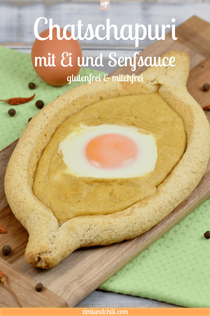 Chatschapuri mit Ei und Senfsauce auf länglichem Holzbrettchen. Heller Hintergrund dekoriert mit einem Ei, getrockneten Chilischoten und Pimentkörnern. Pin beschriftet.