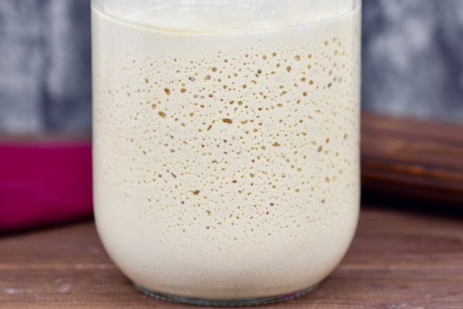 Glutenfreier Sauerteig im Glas. Man sieht die Bläschenbildung. Hintergrund dunkel.