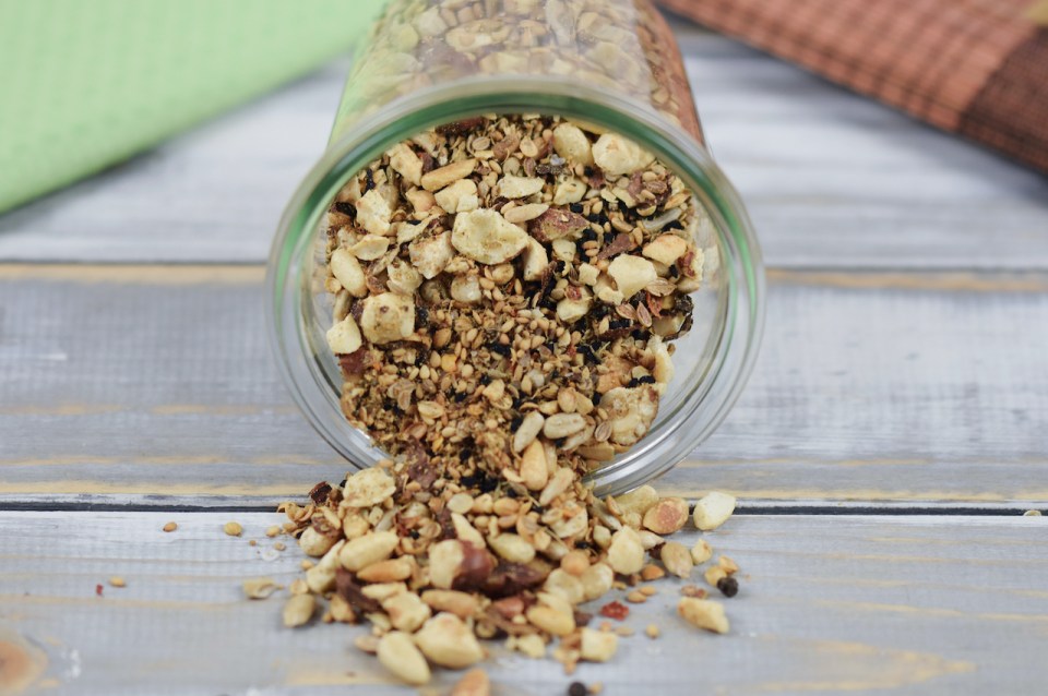 Dukkah selber gemacht in einem liegenden Glas. Etwas Dukkah ist herausgerutscht. Hintergrund hell.