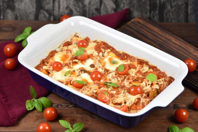 Gnocchi-Auflauf in cremiger Tomatensauce mit Pilzen und Cocktailtomaten in einer Auflaufform. Hintergrund dunkel.