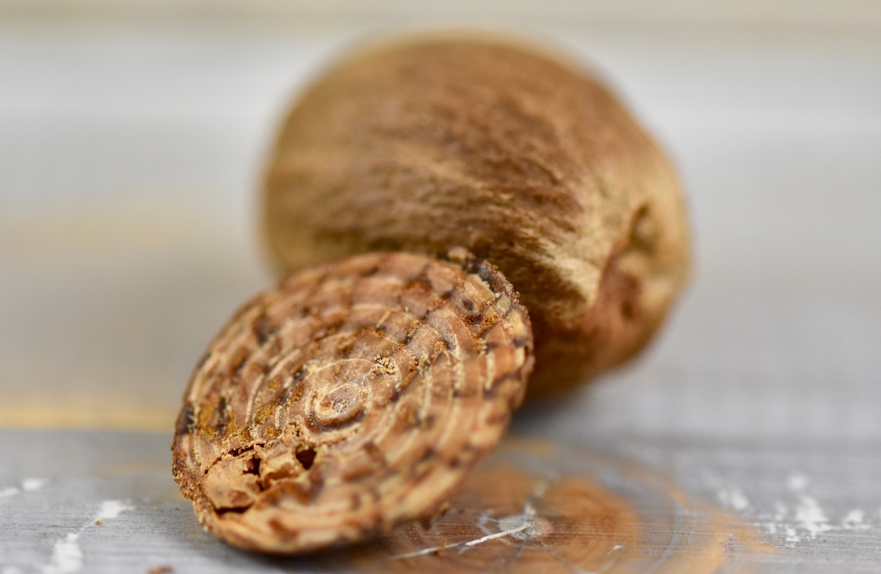 Muskatnüsse, eine ganze und ein Rest einer abgeriebenen Muskatnuss. Hintergrund hell.