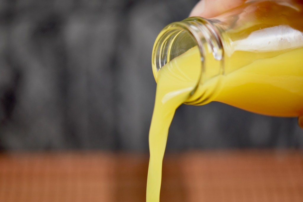 Orangensaft in Glasflasche, wird geschüttet, Hintergrund dunkel