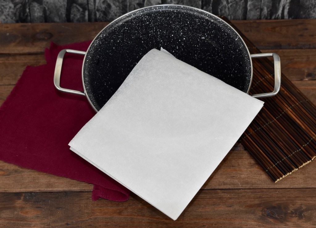 Ein Blatt weißes Backpapier 2 mal gefaltet. Eine Spitze mittig über einen Topf gelegt. Hintergrund dunkel.