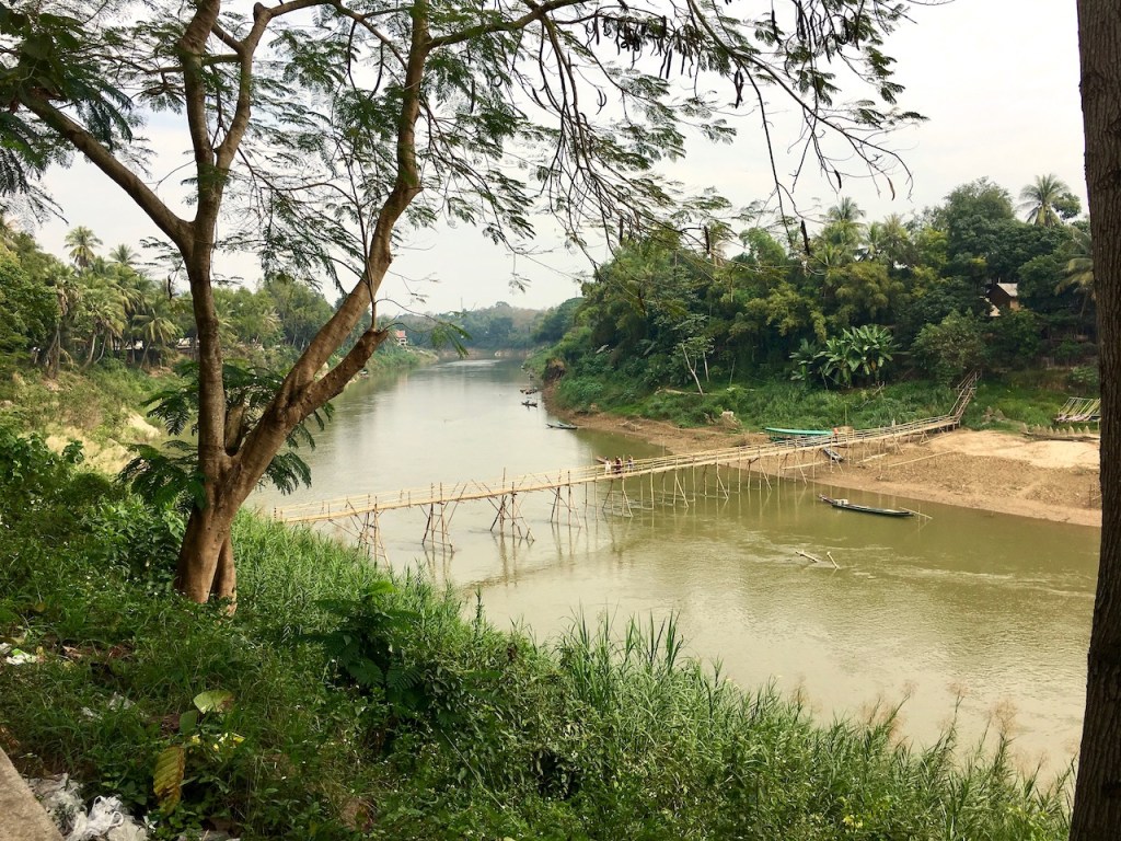 hölzerne Hängebrücke über einem Nebenfluss vom Mekong mit tropischer Vegetation in Luang Prabang - Laos