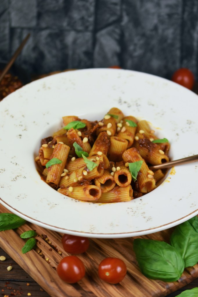 Pasta mit karamellisierten Zwiebeln auf weißem Teller. Hintergrund dunkel.