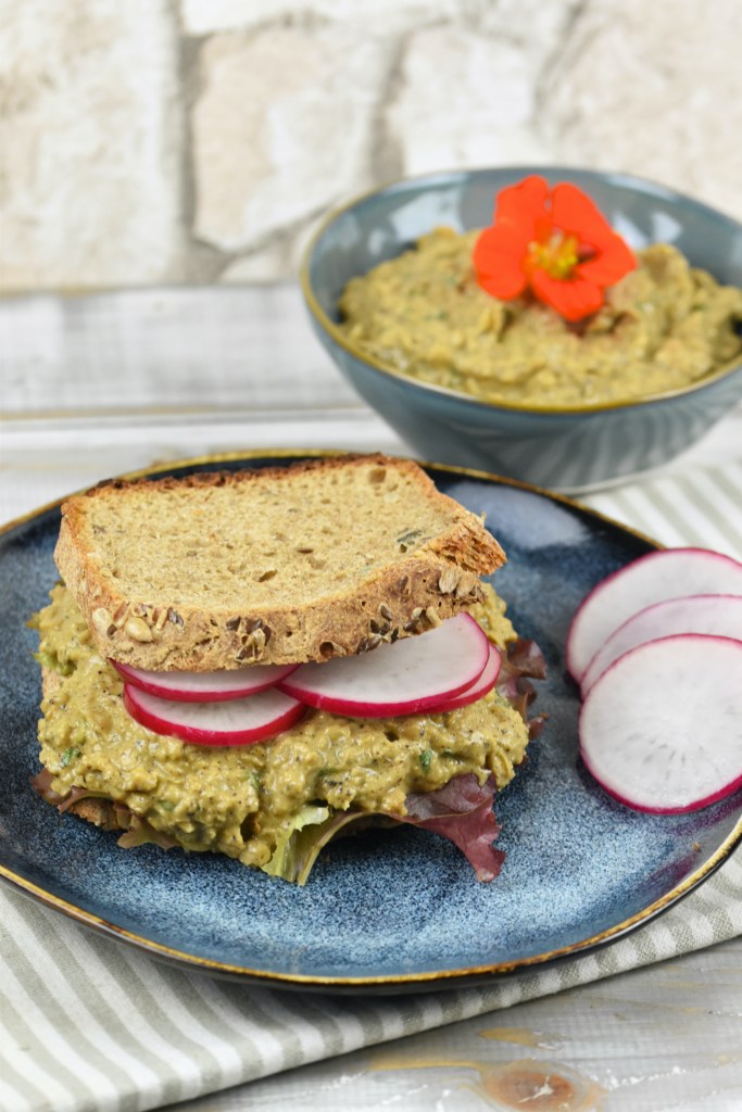 Veganer Thunfischsalat aus Kichererbsen in einer blaugrauen Schale und auf einem Sandwich mit Radieschen